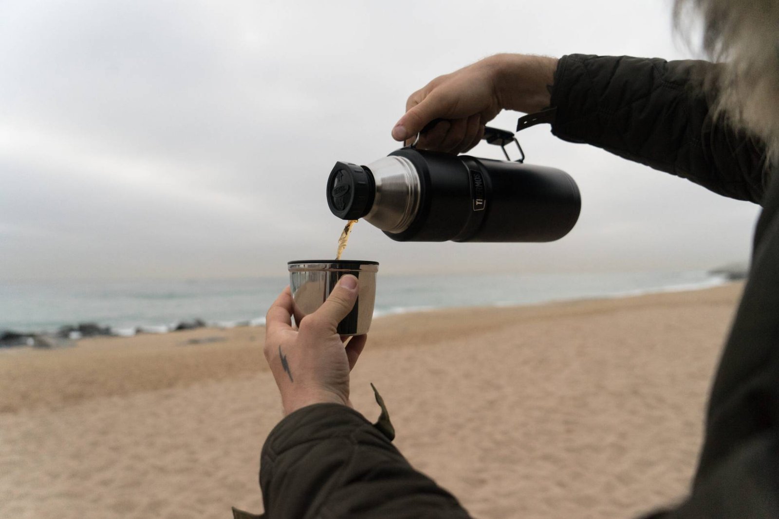 Man Warm Jacket With Hand Tattoos Pours Hot Coffee Tea Into Thermos Insulated Cup Cold Rainy Day Scaled